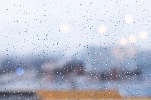 Window in the rain, large drops of rain on the glass, blurred outlines of the city in the background. Abstract background texture