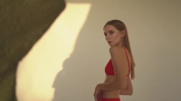 Egy piros alsógatyás lány egy fehér falnak áll. — Stock videók