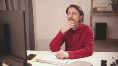 Adam elinde telefonla bilgisayarda yazı yazıyor.