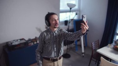 Kulaklıklı ve elinde telefon olan bir adam konuşuyor.