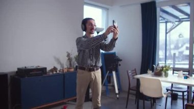 Kulaklıklı ve elinde telefon olan bir adam konuşuyor.