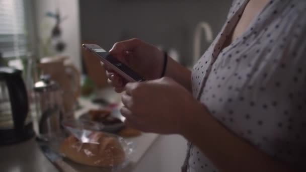 Дівчина на кухні з телефоном в руці — стокове відео