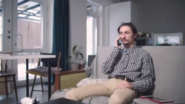 Adam oturur ve telefonda mutlu bir şekilde konuşur.