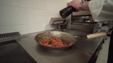 Şef sebze pişirirken baharat ekliyor.