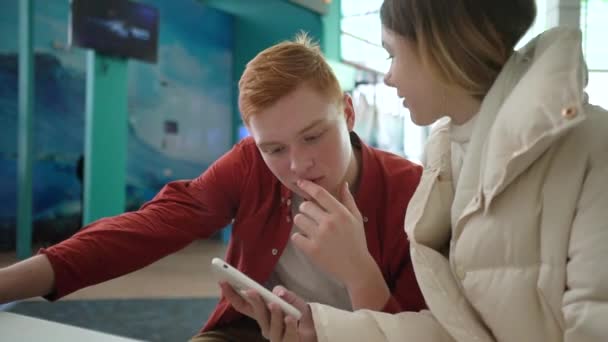 Férfi a lány telefonnal a kezében csevegés a kávézóban — Stock videók