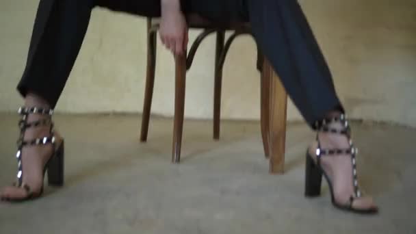 Девушка в черных туфлях сидит на стуле — стоковое видео