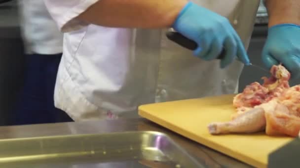 Un chef con guantes azules corta un pollo en una tabla de cortar — Vídeos de Stock