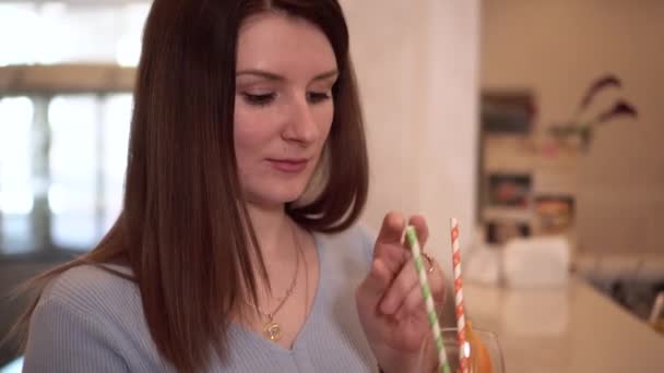 Молодая брюнетка с длинными волосами пьет коктейль из стакана с соломинкой. — стоковое видео