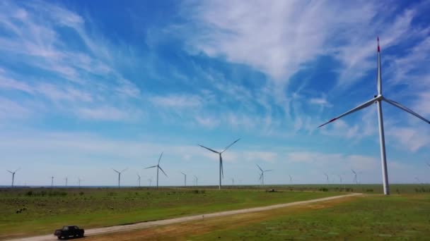 The car is driving along a rural road, among large wind turbines — Wideo stockowe