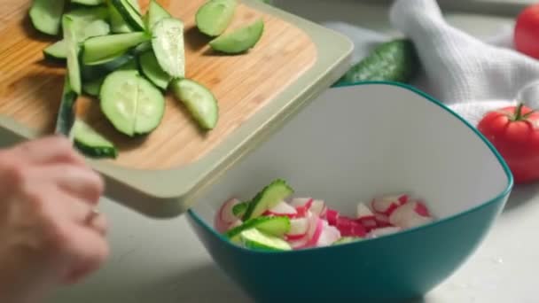 Шеф-повар добавляет нарезанные огурцы в овощной салат — стоковое видео