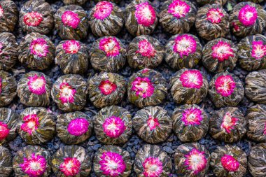 Yüksek çözünürlüklü, kurumuş yeşil çay yaprakları ve pembe çiçeklerden yapılmış çiçek çay topları. Bu dokulu desen bitki çayı, geleneksel çay kültürü, rahatlama, sağlık, doğal ürünler ve gurme içeceği bileşenlerini temsil eder..