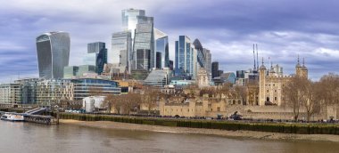 Londra 'nın panoramik manzarası Londra' nın tarihi kulesini modern şehir finans bölgesinin yanında gösteriyor. Thames nehri boyunca yükselen gökdelenler dramatik bulutlu gökyüzünün altında, miras ve çağdaş mimarinin zıtlığını vurguluyor..
