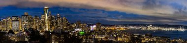 Seattle 'ın gece manzarası, ikonik uzay iğnesi ile modern şehir merkezindeki gökdelenlerle çevrili. Sıcak şehir ışıkları, derin mavi bulutlarla tezat oluşturarak seyahat, finans, teknoloji ve metropol kavramları için mükemmel bir şehir atmosferi yaratır..