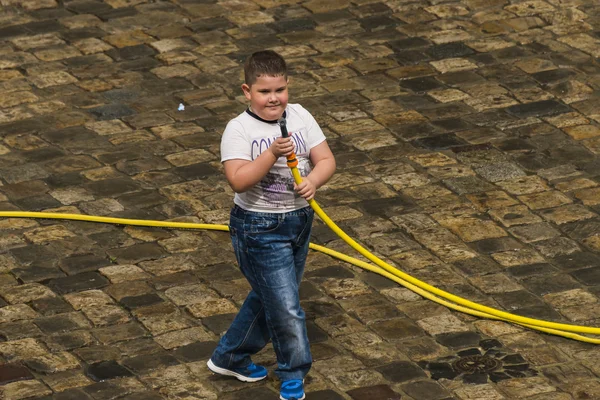 Feliz chico vierte agua de una manguera transeúntes . — Foto de Stock