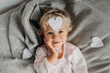 Kıvırcık bir bebeğin kafasında beyaz kağıt bir kalp. Sevgililer Günü konsepti.