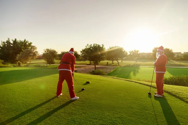 Gün batımında golf oynayan iki Noel Baba.