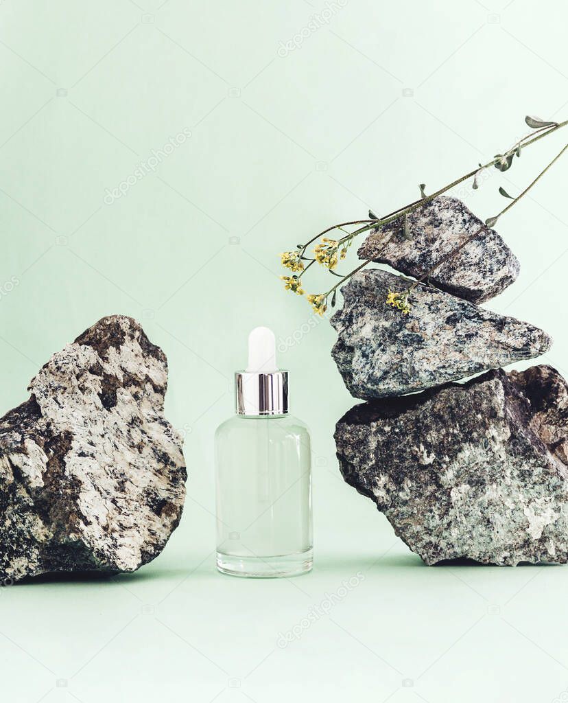 Serum or oil In glass bottle with pipette with stones on green background.
