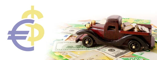 wooden car with coins on euro and dollars texture background panorama