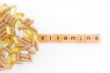 Farklı hapların beyaz arka planında tahta küplere kazınmış vitaminler.