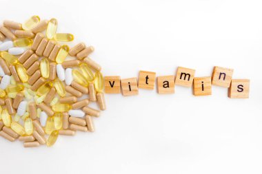 Farklı hapların beyaz arka planında tahta küplere kazınmış vitaminler.