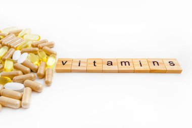 Farklı hapların beyaz arka planında tahta küplere kazınmış vitaminler.