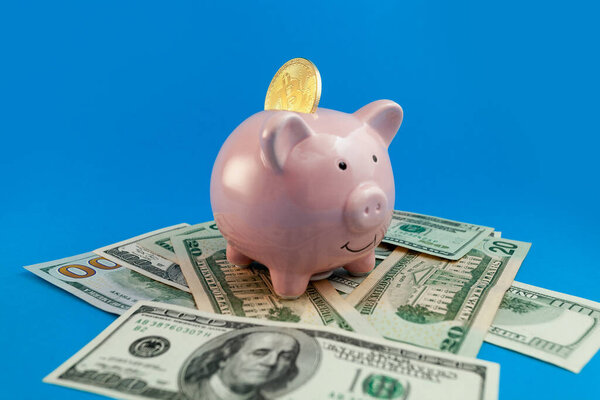 копилка с монетой на фоне банкнот в долларах США на синем фоне