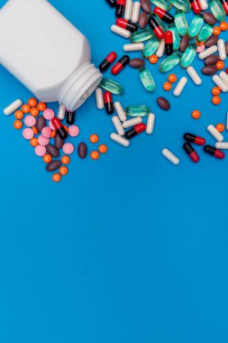 Mavi arka planda kavanozdan düşen çok renkli haplar.