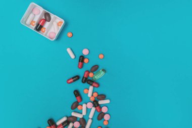 Mavi arka planda çok renkli hapları olan ilaç dağıtıcısı.