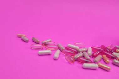 Pembe arka planda çok renkli haplar ve kapsüller.