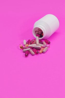 Pembe arka planda çok renkli haplar ve kapsüller.