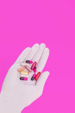 Pembe arka planda çok renkli haplar ve kapsüllerden oluşan bir eldiven verin.
