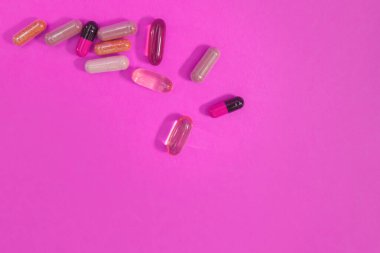 Pembe arka planda çok renkli haplar ve kapsüller.