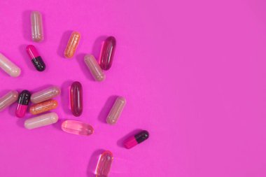 Pembe arka planda çok renkli haplar ve kapsüller.