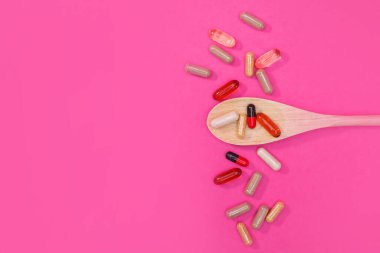 Pembe arka planda çok renkli haplar ve kapsüller.