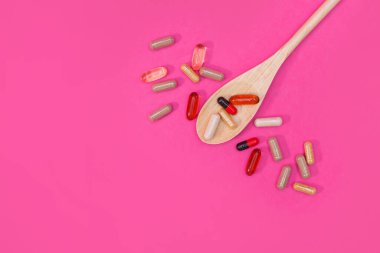 Pembe arka planda çok renkli haplar ve kapsüller.