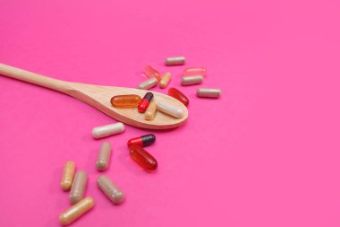 Pembe arka planda çok renkli haplar ve kapsüller.