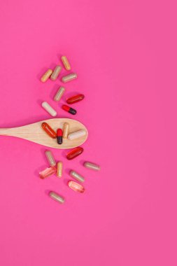 Pembe arka planda çok renkli haplar ve kapsüller.