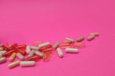 Pembe arka planda çok renkli haplar ve kapsüller.