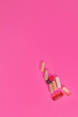 Pembe arka planda çok renkli haplar ve kapsüller.
