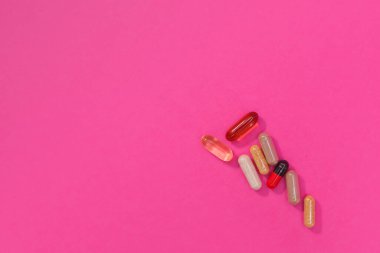 Pembe arka planda çok renkli haplar ve kapsüller.