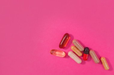 Pembe arka planda çok renkli haplar ve kapsüller.
