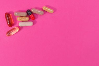Pembe arka planda çok renkli haplar ve kapsüller.