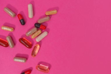 Pembe arka planda çok renkli haplar ve kapsüller.