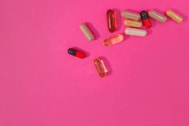 Pembe arka planda çok renkli haplar ve kapsüller.
