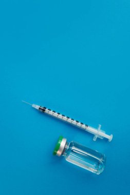 Mavi zemin üzerinde ilaç bulunan şırınga ampulü