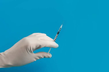 Mavi arka planda şırınga ve ampul bulunan bir eldiven verin.