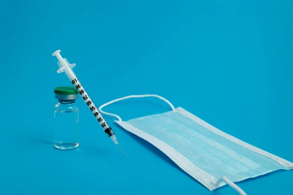 syringe, medical mask and ampoule with medicine on a blue background