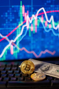 Grafiklerin arkaplanındaki bir bilgisayar klavyesinde kum saati, dolar ve bitcoin 'ler