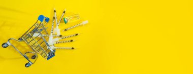Sarı panorama arka planında şırınga ve ampul bulunan süpermarket arabası