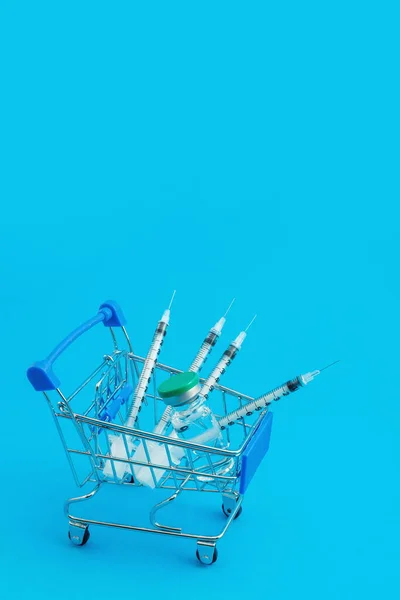 青い背景に注射器とアンプルが付いたスーパーマーケットのトロリー — ストック写真